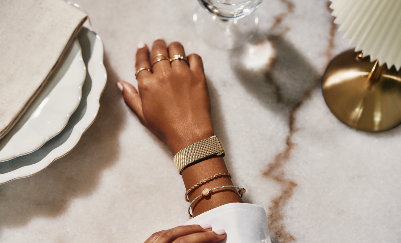 Fitbit Air met gouden Metal Mesh-bandje om de pols op een marmeren tafel