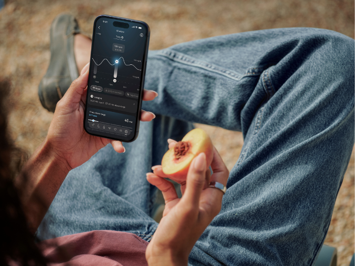 Persoon houdt een iPhone met de Oura-app vast en eet een perzik